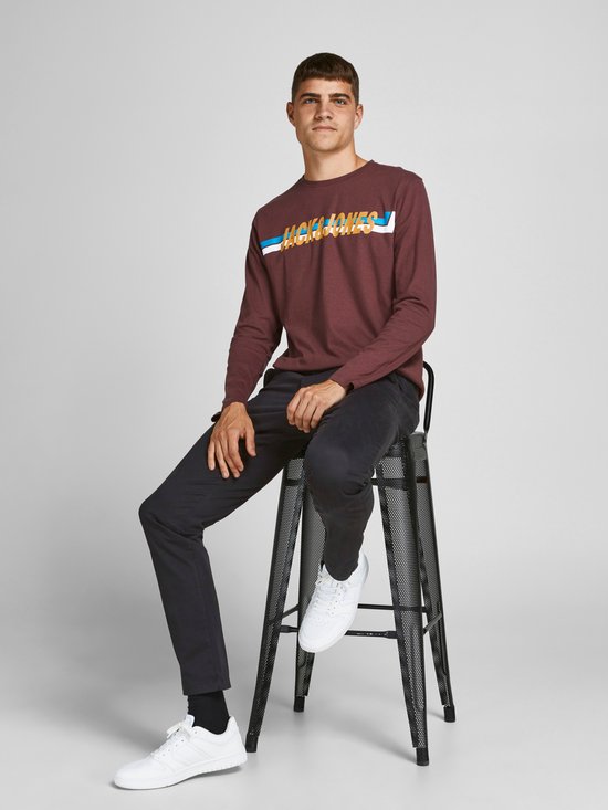 Man zittend op een stoel, met op zijn bordeauxrode shirt 'JACK&JONES' in kleurrijke letters.
