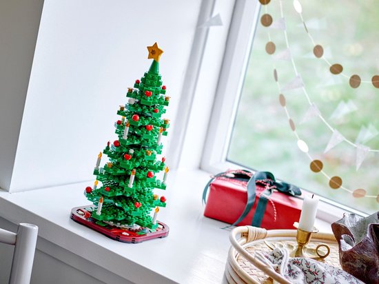 Sapin de Noël LEGO vert avec boules rouges, bougies blanches et étoile jaune sur rebord de fenêtre près d'un cadeau.