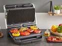 Open contactgrill met gegrilde paprika's in verschillende kleuren (rood, geel, oranje) op de grillplaten.