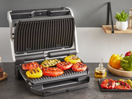 Open contactgrill met gegrilde paprika's in verschillende kleuren (rood, geel, oranje) op de grillplaten.