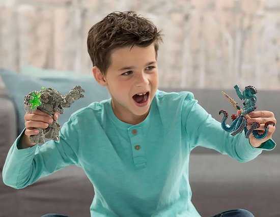 Een jongen met een lichtblauwe trui speelt met een stenen monster en een blauwe octopus figuur.