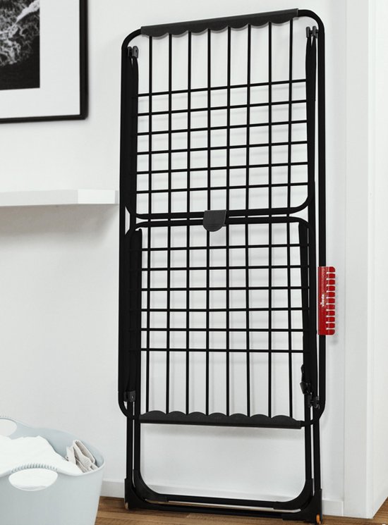 Étendage noir pliable debout contre un mur blanc avec un accessoire Vileda rouge.