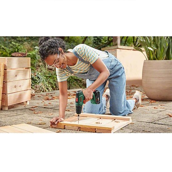 Vrouw metoverall en Bosch EasyDrill 18V-40 accuboormachine boort in houten planken.