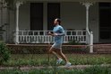 Man in blauw shirt en grijze shorts rent langs een huis met een zwart Garmin smartwatch om de pols.