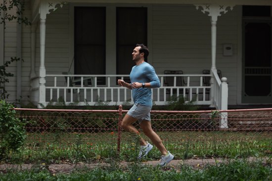 Man in blauw shirt en grijze shorts rent langs een huis met een zwart Garmin smartwatch om de pols.
