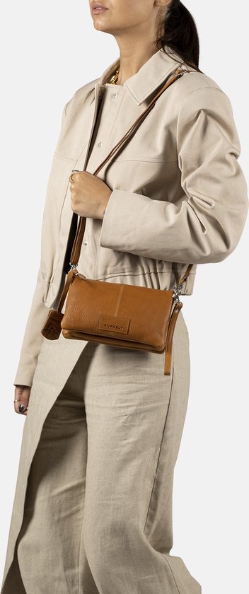 Bruine leren schoudertas gedragen door een model met beige kleding.