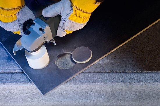 Gouden handschoenen gebruiken een haakse slijper met een diamantboorkop om een gat te maken in een donker oppervlak.