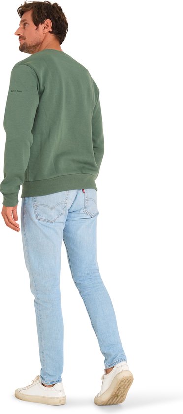Man met lichtblauwe jeans en een mosgroene trui. De trui heeft een subtiele, geborduurde tekst op de mouw.