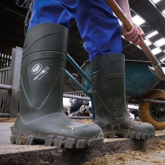 Boer in blauwe broek draagt groene Bekina werklaarzen in stal.