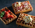 Drie goudbruine wafels met toppings: aardbeien, marshmallows, ijs, slagroom en amandelen.