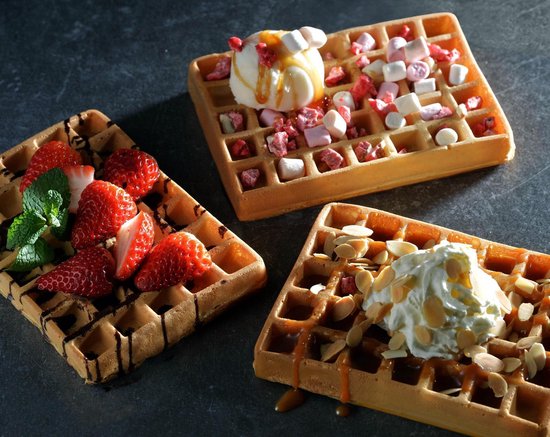 Drie goudbruine wafels met toppings: aardbeien, marshmallows, ijs, slagroom en amandelen.