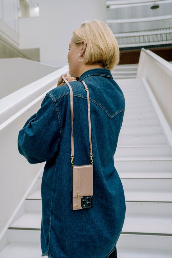 Vrouw met spijkerjack draagt een roze telefoonhoesje met koord om haar nek.