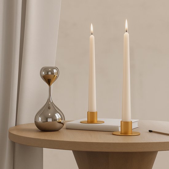 Twee witte kaarsen in gouden kaarthouders op een houten tafel naast een zilveren vaas.