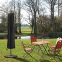 Zwarte parasolhoes naast een tuintafel en stoelen in een parkachtige omgeving.