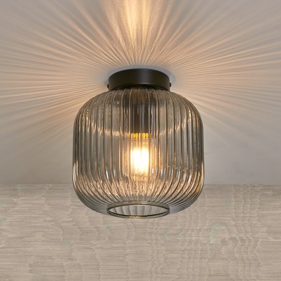 Plafondlamp met geribbeld rookglas en donkergrijs armatuur, projecteert lichtpatronen op het plafond.