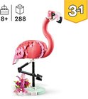 Een roze LEGO flamingo op één poot met een groene basis en paarse bloemen.
