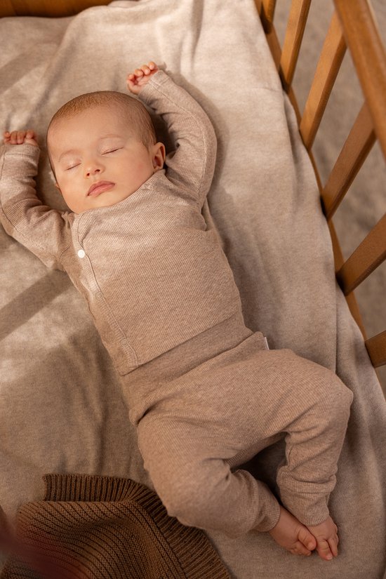 Slapende baby in een wieg, gekleed in een taupe melange longsleeve en broek, liggend op een taupe deken.