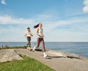 Twee vrouwen rennen langs de kustlijn met op de voorgrond een vrouw in een blauw sport-topje en bruine legging.