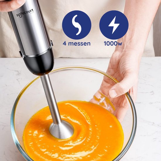 Handen gebruiken een zilverkleurige staafmixer om een oranje soep te pureren in een glazen kom. "4 messen, 1000W."