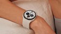 Witte smartwatch met een zilverkleurige rand, gedragen op een arm. Het scherm toont diverse widgets.
