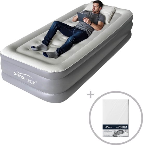 Man ligt op een grijs en wit Aerorest luchtbed met kussen en tablet, naast een verpakking van een wit hoeslaken.