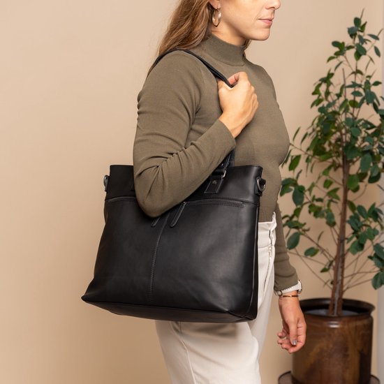 Vrouw draagt een zwarte lederen tas met handvatten en een schouderband.