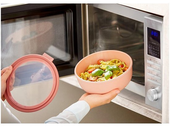 Een hand haalt een roze kom met pasta uit een magnetron.