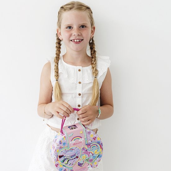 Une fille souriante avec des tresses, tenant un coffret créatif en forme de cœur sur le thème de la licorne.