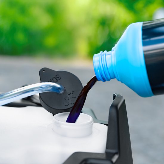Paars reinigingsmiddel wordt uit een blauwe fles gegoten in de watertank van een hogedrukreiniger.