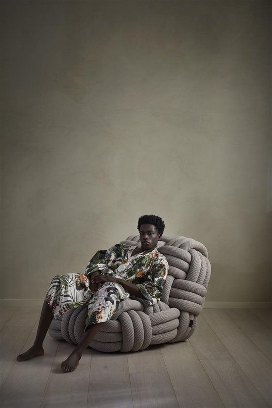 Model zit op een grijze stoel, gekleed in een lichte badjas met veelkleurige jungleprint.