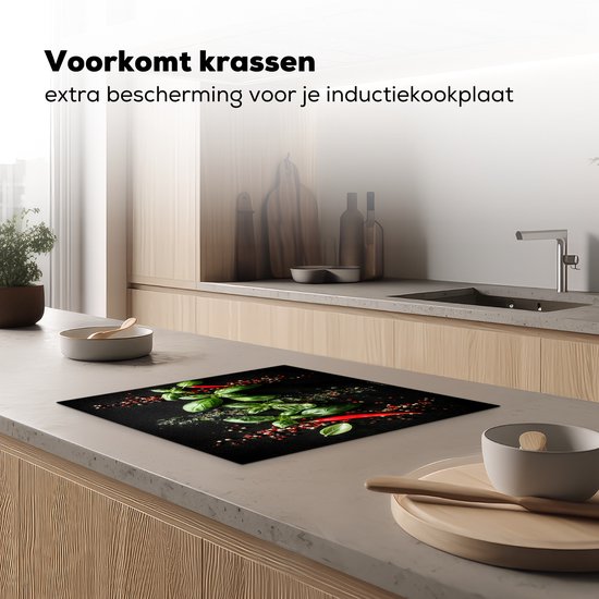Zwarte inductiebeschermer met basilicum, pepers en kruiden op een inductiekookplaat in een keuken.