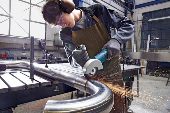 Jonge man met gehoorbescherming slijpt een metalen buis met een Bosch haakse slijper.