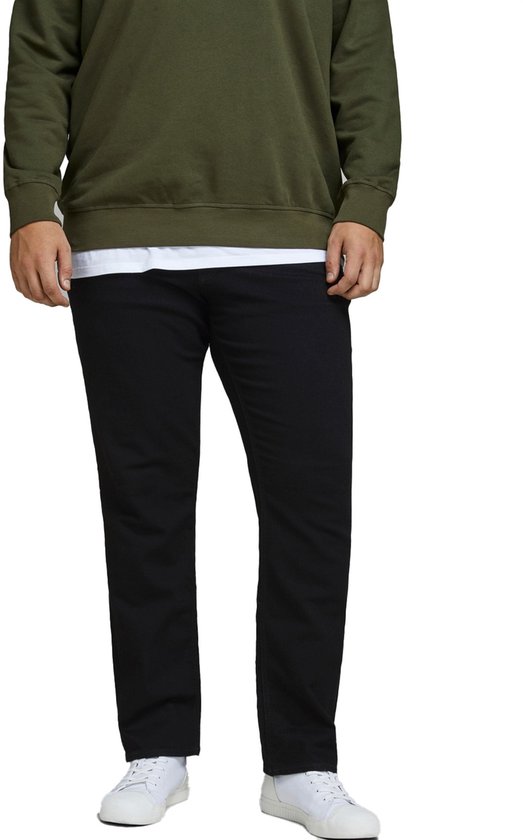 Man met olijfgroene sweater en zwarte jeans, staand.