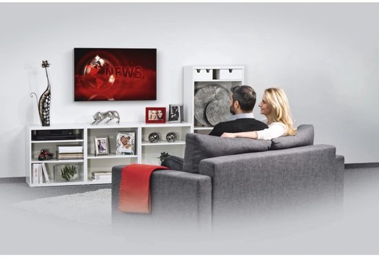 Een koppel zit op een grijze bank en kijkt naar een zwarte TV met nieuws op het scherm.