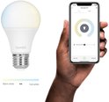 Hand met smartphone, Hombli app 'Smart Bulb CCT' bedient lamp. Lamp met logo 'Hombli' naast de telefoon.