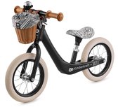 Zwarte loopfiets met rieten mandje, bruine handvatten, zadel met zwart-wit patroon, crèmekleurige banden.