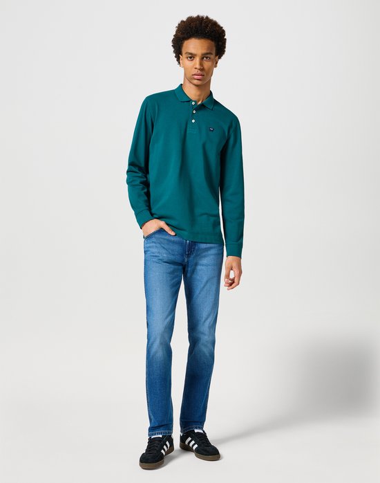 Model draagt een langemouw polo in groen en een blauwe Wrangler Greensboro jeans.