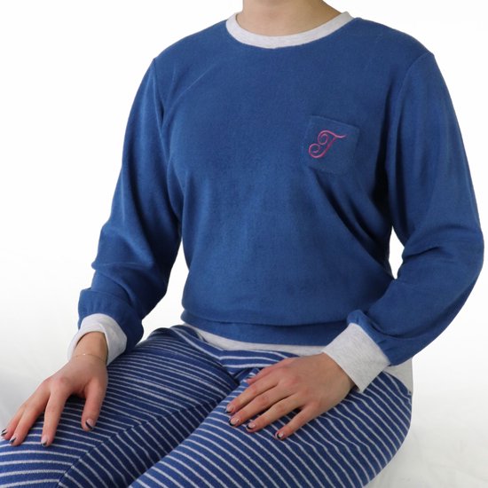 Model in blauwe pyjamatop van badstof met monogram 'T' en gestreepte pyjamabroek.