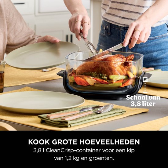 Grote glazen schaal met kip en groenten, bij een eettafel met mensen die snijden.