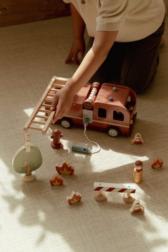 Kind speelt met houten brandweerwagen, ladder, boom, poppetjes, hydrant en vuurelementen.