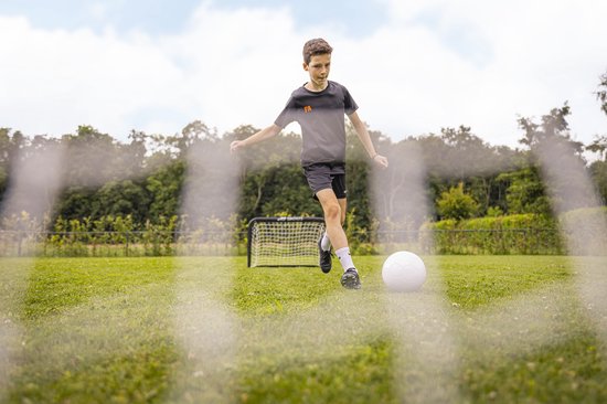 Jongen traint voetbal op grasveld met voetbaldoel van AJ-Sports op de achtergrond.