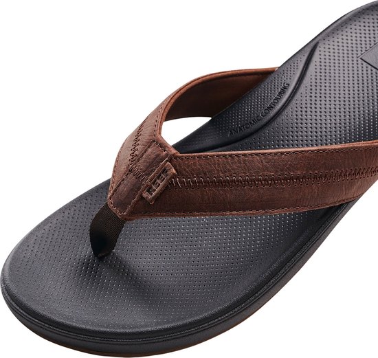 Bruine leren Reef slipper met zwart, anatomisch gevormd voetbed en tekst 'ANATOMIC CONTOURING'.