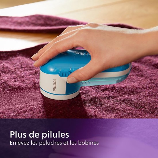Hand gebruikt een lichtblauwe Philips pluizenverwijderaar om pluizen van een paars kledingstuk te verwijderen.
