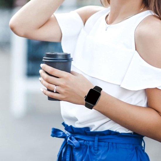 Een vrouw met een zwarte smartwatchband om haar pols, terwijl ze een kop koffie vasthoudt.