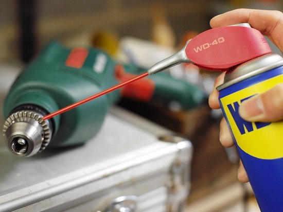 Hand spuit WD-40 met rode sproeibuis in boor van groene boormachine.
