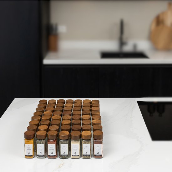 Rangée de 42 pots d'herbes en verre avec couvercles en acacia sur un plan de travail blanc.