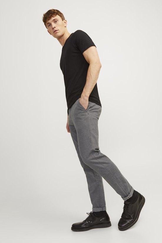 Man draagt zwarte t-shirt en grijze broek met fijne structuur, in een dynamische pose.