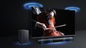 Man luistert op bank naar cellist op tv, met soundbar en subwoofer die geluid verspreiden.