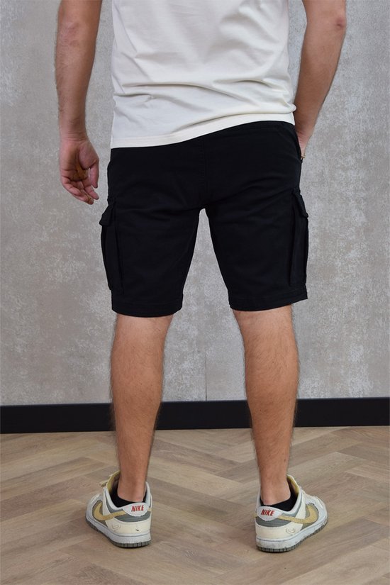 Man in zwarte cargobroek met klepzakken, gedragen met een witte top en sneakers.