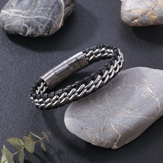 Zwart gevlochten leren armband met dubbele zilverkleurige schakelketting, rustend op stenen.